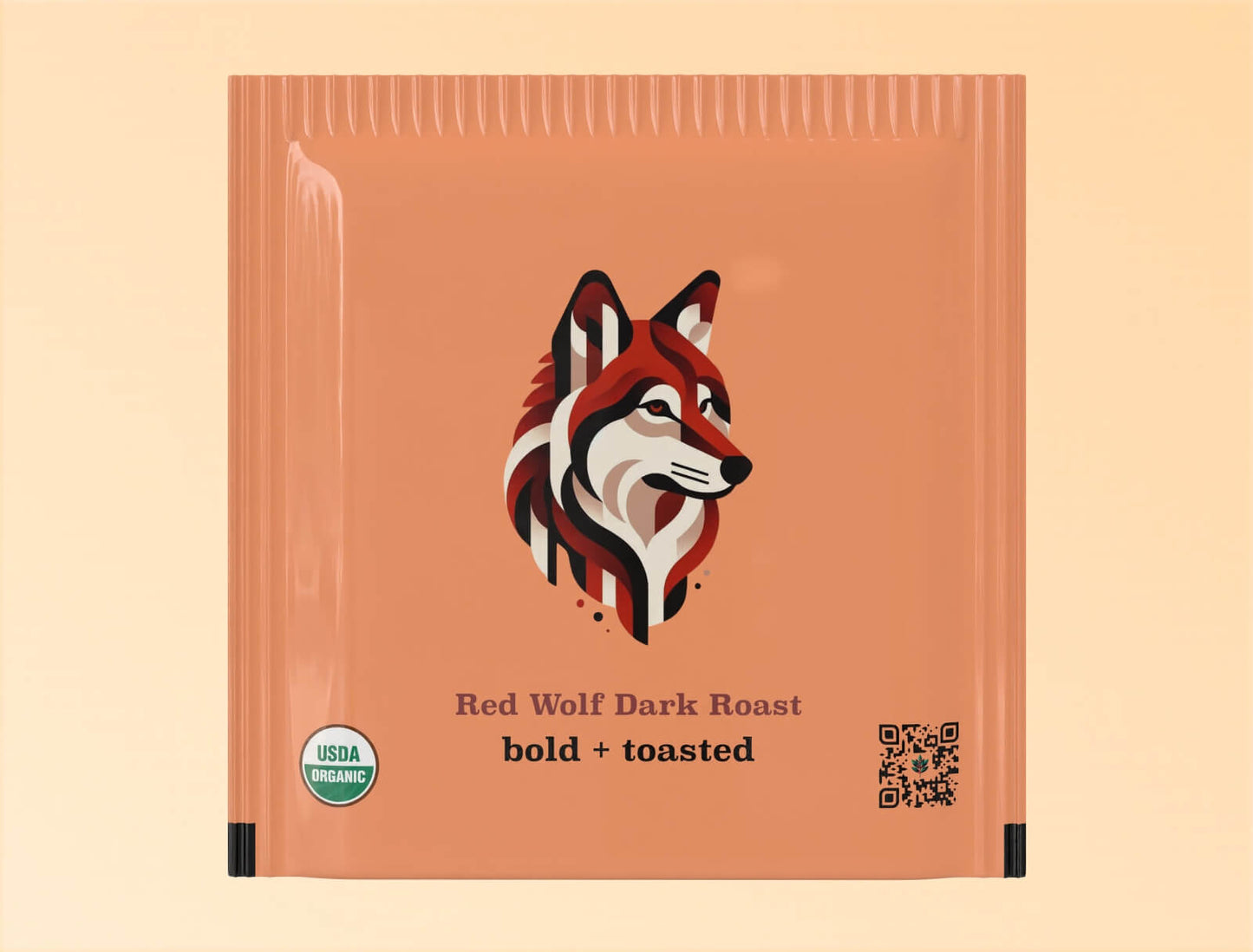 "Individual teabag packaging for Goldholly's Red Wolf Dark Roast yaupon tea. The terracotta-colored sachet features a geometric, color-blocked illustration of a red wolf head in profile against the warm background. Below the illustration are the words 'Red Wolf Dark Roast' and 'bold + toasted' in dark typography. The package includes a USDA Organic certification seal and QR code.