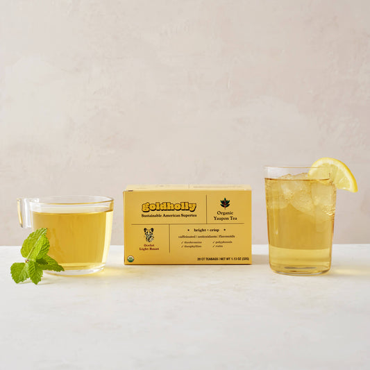 Goldholly Ocelot Light Roast box with clear glass mugs filled with golden yaupon tea on clean white marble surface. Fresh mint garnish and lemon slice enhance the bright, crisp flavor profile of America's only native caffeinated plant.