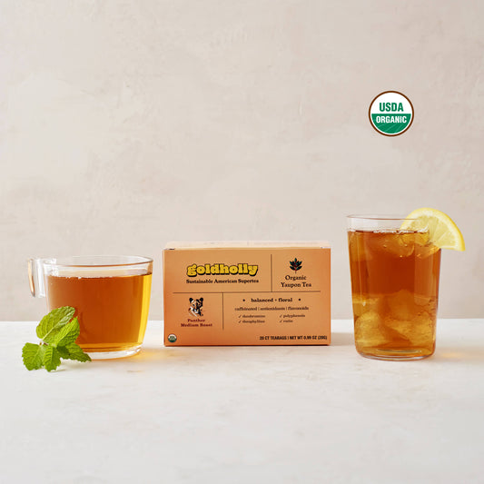 Goldholly Panther Medium Roast box with glass mugs of rich amber yaupon tea garnished with fresh mint and lemon, with the USDA Certified Organic seal in the upper right side of the image. Balanced, floral notes shine through in this elegant product styling.