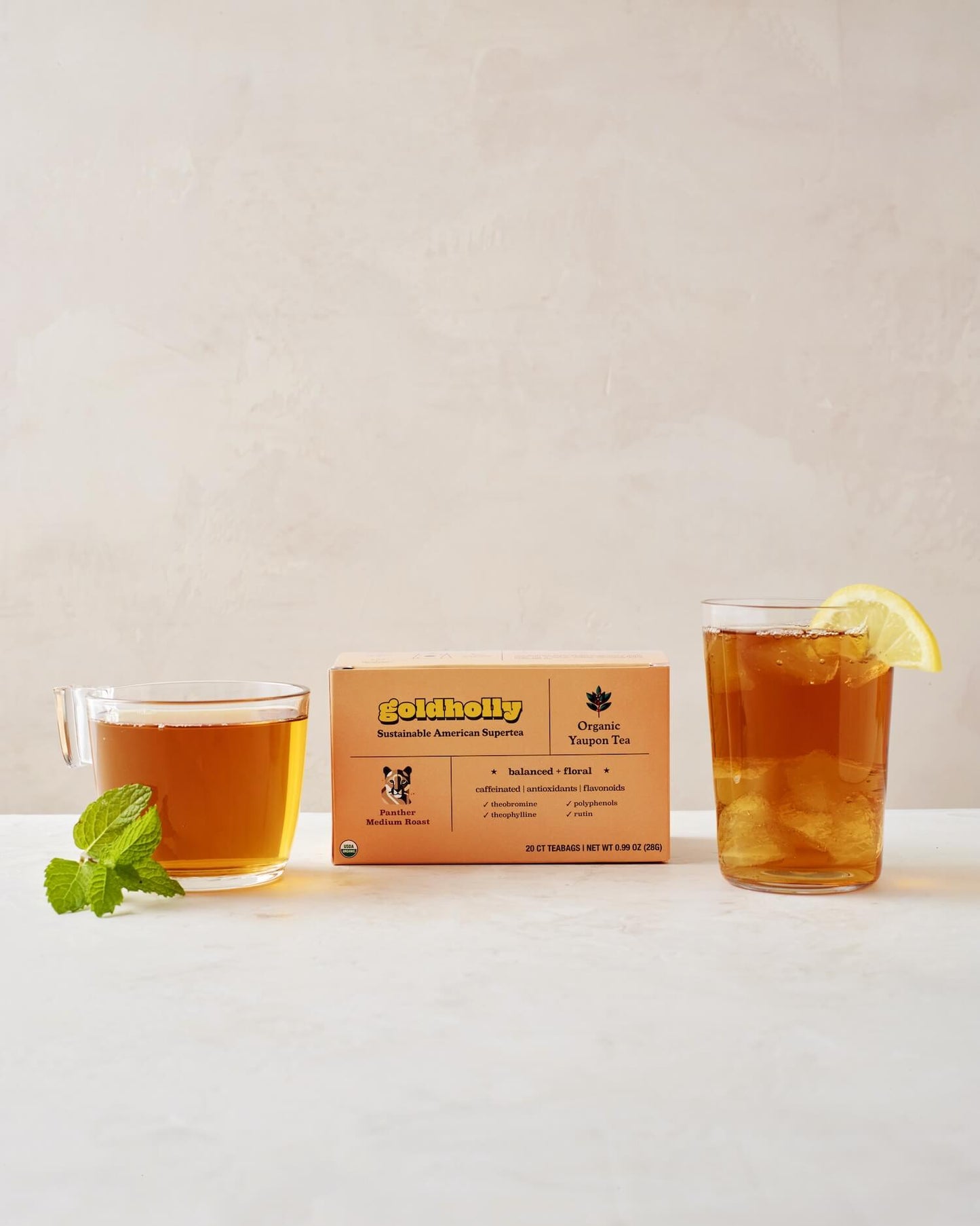 Goldholly Panther Medium Roast box with glass mugs of rich amber yaupon tea garnished with fresh mint and lemon. Balanced, floral notes shine through in this elegant product styling.