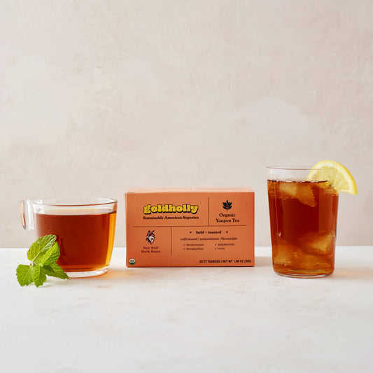 Goldholly Red Wolf Dark Roast box with glass mugs of deep amber yaupon tea garnished with fresh mint and lemon. Bold, toasted flavor profile perfect for rich, satisfying caffeine experience.
