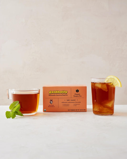 Goldholly Red Wolf Dark Roast box with glass mugs of deep amber yaupon tea garnished with fresh mint and lemon. Bold, toasted flavor profile perfect for rich, satisfying caffeine experience.