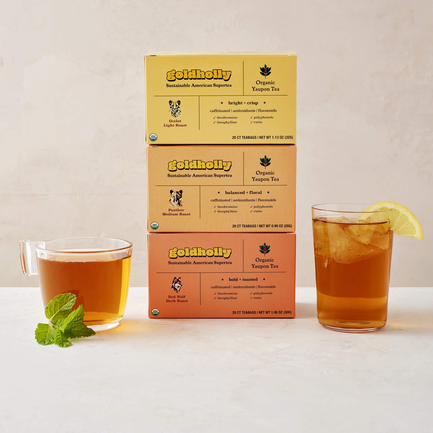 Goldholly three-roast bundle pack featuring stacked boxes of Ocelot Light, Panther Medium, and Red Wolf Dark Roast with glass mugs of amber yaupon tea. Complete collection showcases the full spectrum of America's native caffeine flavors from bright to bold.