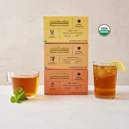 Goldholly three-roast bundle pack featuring stacked boxes of Ocelot Light, Panther Medium, and Red Wolf Dark Roast with glass mugs of amber yaupon tea, with the USDA Certified Organic seal in the upper right side of the image. Complete collection showcases the full spectrum of America's native caffeine flavors from bright to bold.