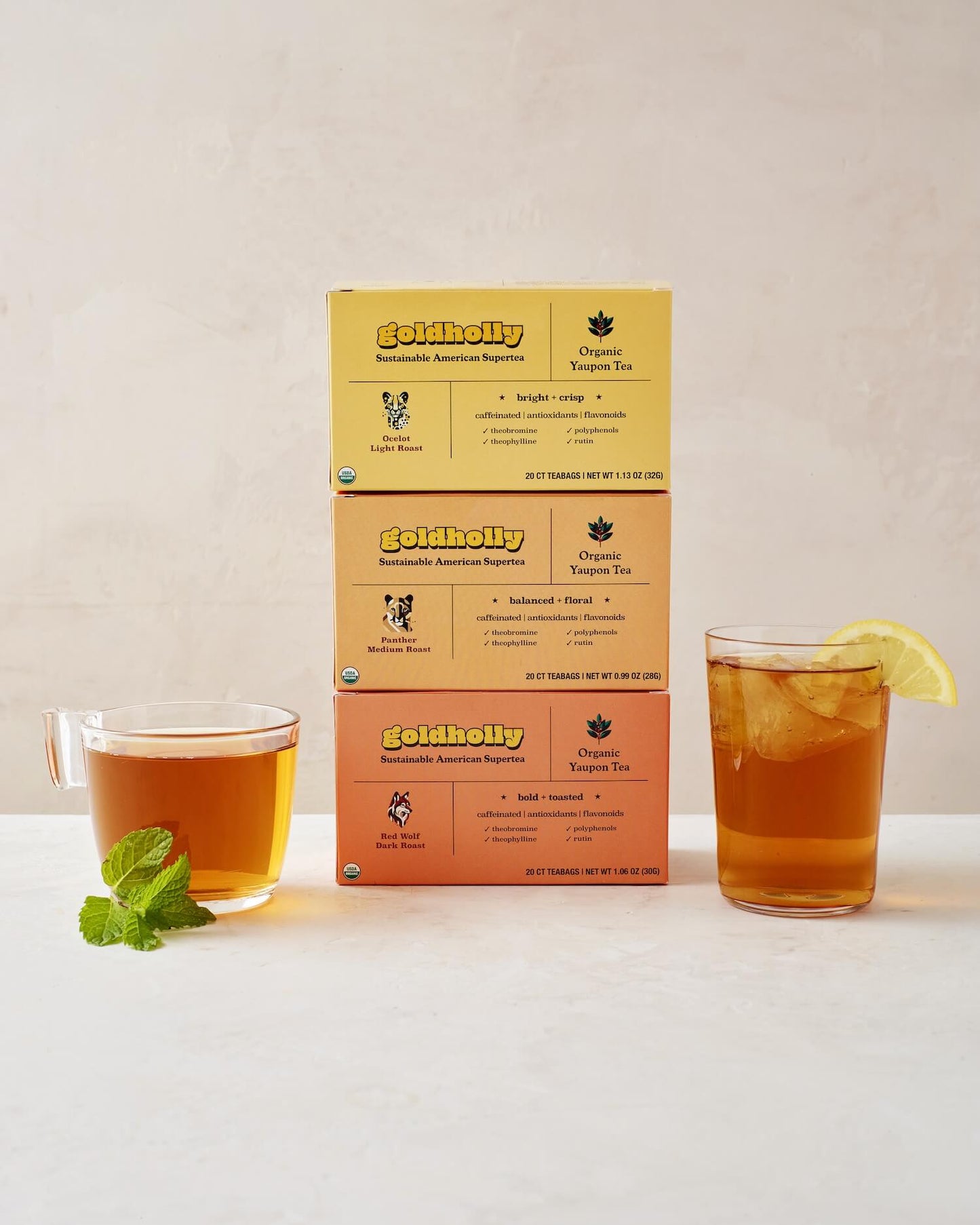 Goldholly three-roast bundle pack featuring stacked boxes of Ocelot Light, Panther Medium, and Red Wolf Dark Roast with glass mugs of amber yaupon tea. Complete collection showcases the full spectrum of America's native caffeine flavors from bright to bold.