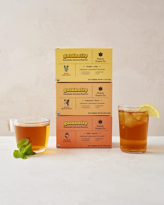 Goldholly three-roast bundle pack featuring stacked boxes of Ocelot Light, Panther Medium, and Red Wolf Dark Roast with glass mugs of amber yaupon tea. Complete collection showcases the full spectrum of America's native caffeine flavors from bright to bold.