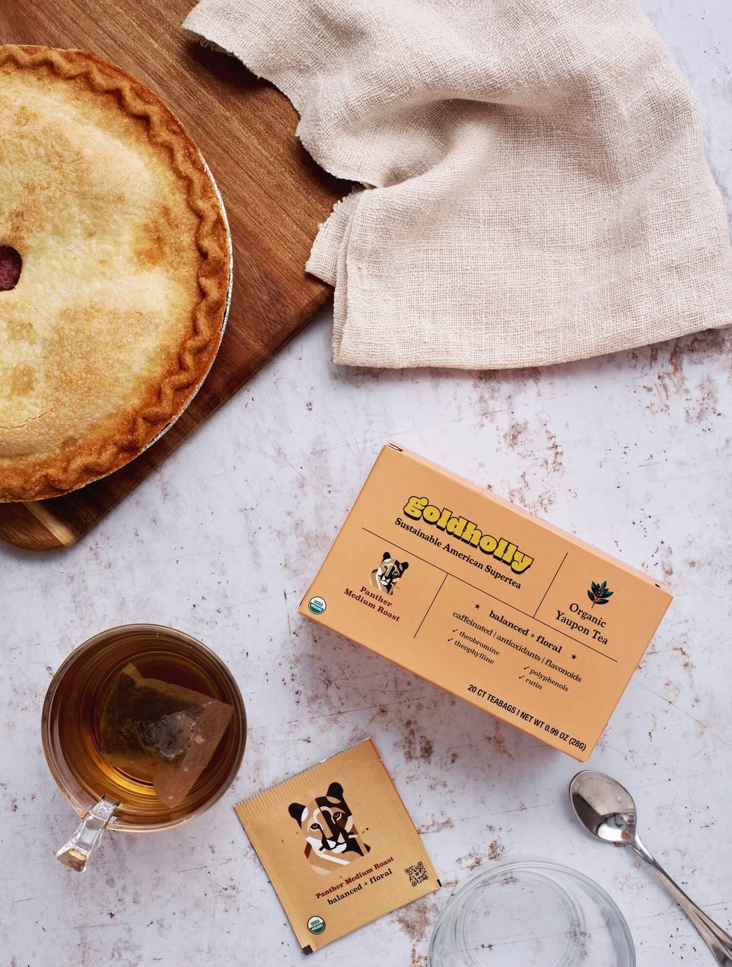 Morning breakfast scene with Goldholly Panther Medium Roast tea cups paired with golden pastry on marble surface. Soft linen napkin creates cozy atmosphere for enjoying balanced, floral yaupon flavors.