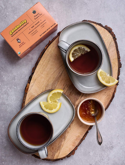 Artisanal tea service with Goldholly Red Wolf Dark Roast in handcrafted ceramic cup on natural wood tray. Rustic pottery and golden honey create sophisticated presentation for bold yaupon tea.