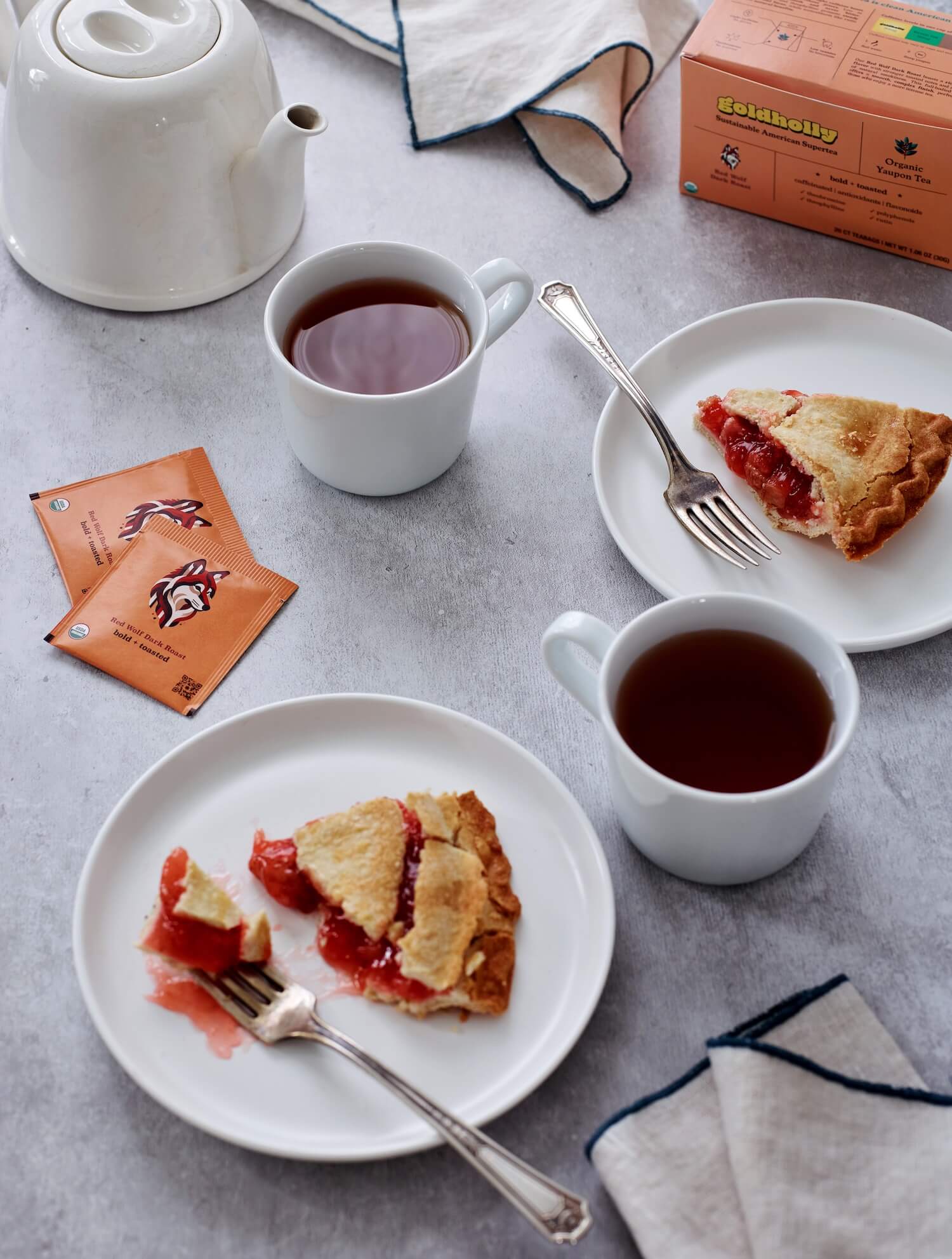Elegant afternoon tea service with Goldholly Red Wolf Dark Roast, white porcelain teapot, and cherry pie. Refined presentation showcases the sophisticated depth of dark-roasted yaupon.