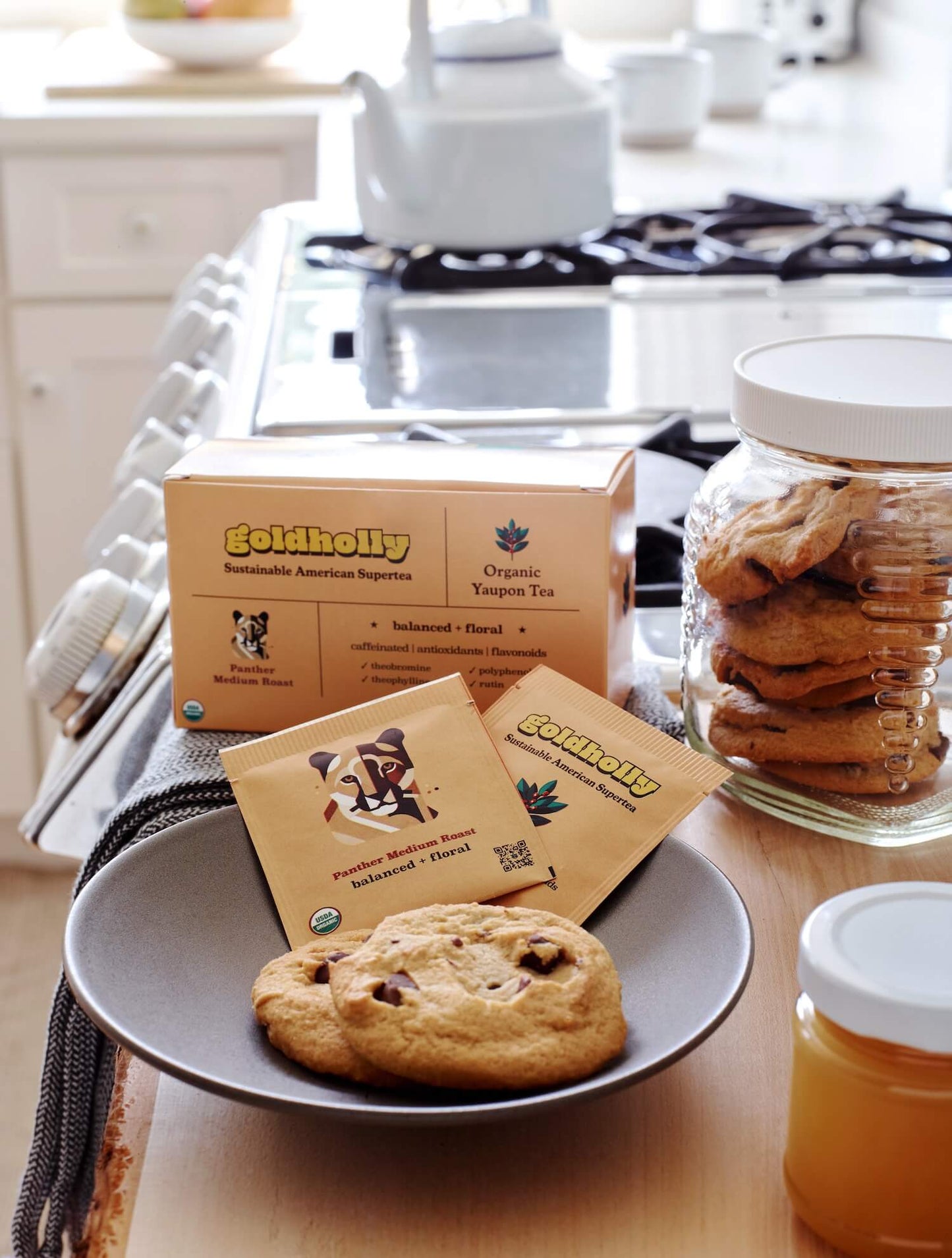 Bright kitchen counter with Goldholly Panther Medium Roast teabags and white ceramic mugs beside fresh-baked cookies. Natural morning light highlights the warm, inviting ritual of sustainable tea brewing.