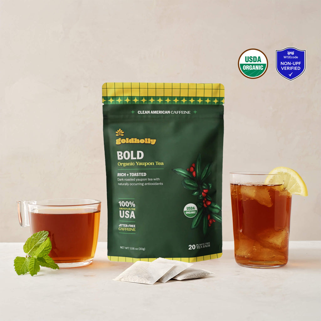 Goldholly Bold organic yaupon tea pouch in deep green with Rich + Toasted flavor tag, flanked by a warm cup of dark brewed tea with mint and an iced glass with lemon, with three teabags. USDA Organic certified and WISEcode Non-UPF verified.--1