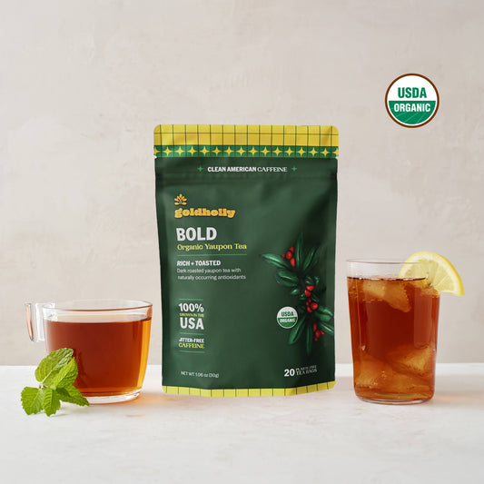 Goldholly Bold organic yaupon tea pouch in deep green with Rich + Toasted flavor tag, flanked by a warm cup of dark brewed tea with mint and an iced glass with lemon, USDA Organic certified