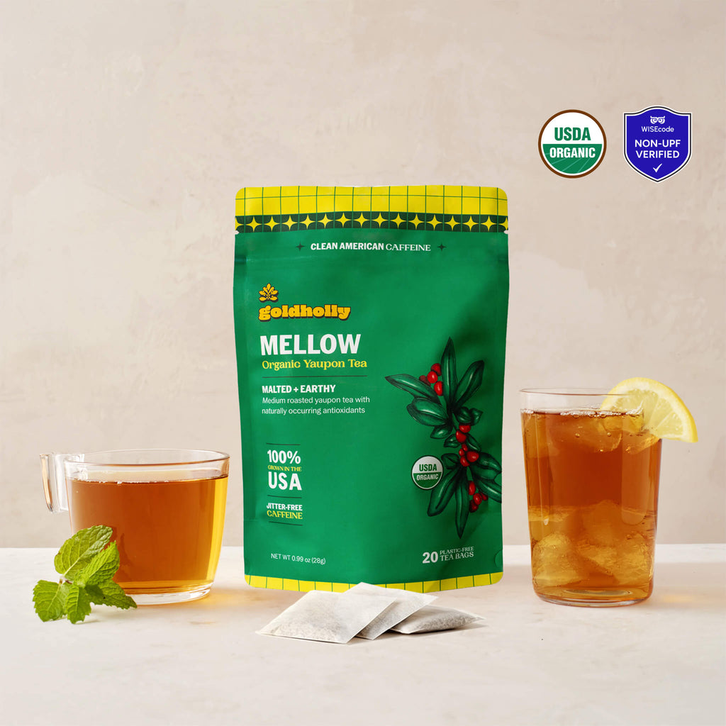 Goldholly Mellow organic yaupon tea pouch in vibrant green with Malted + Earthy flavor tag, flanked by a warm cup of brewed tea with mint and an iced glass with lemon, with three teabags. USDA Organic certified and WISEcode Non-UPF verified.--1