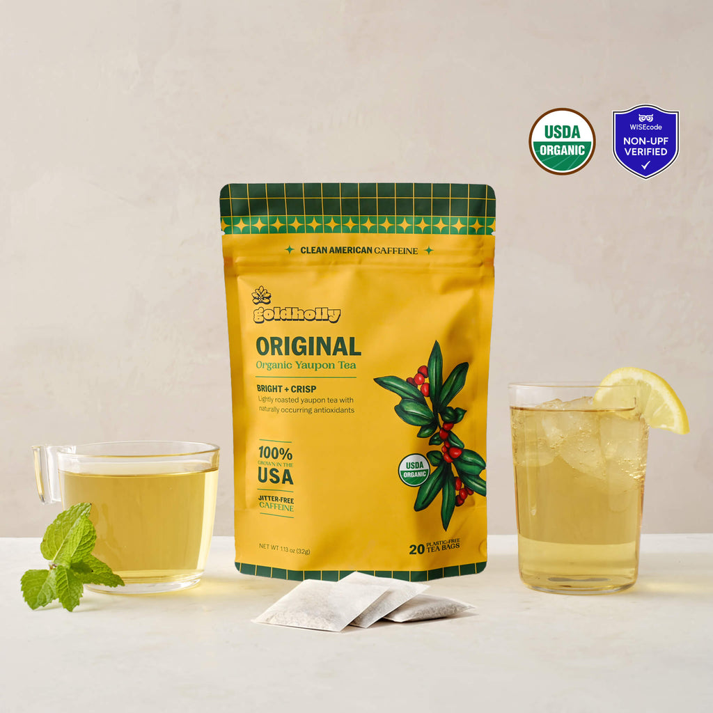 Goldholly Original organic yaupon tea pouch in golden yellow with Bright + Crisp flavor tag, flanked by a warm brewed cup with mint and an iced glass with lemon, with three teabags. USDA Organic certified and WISEcode Non-UPF verified.--1