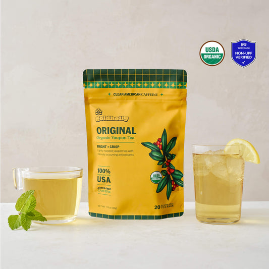 Goldholly Original organic yaupon tea pouch in golden yellow with Bright + Crisp flavor tag, flanked by a warm brewed cup with mint and an iced glass with lemon, USDA Organic and WISEcode Non-UPF verified