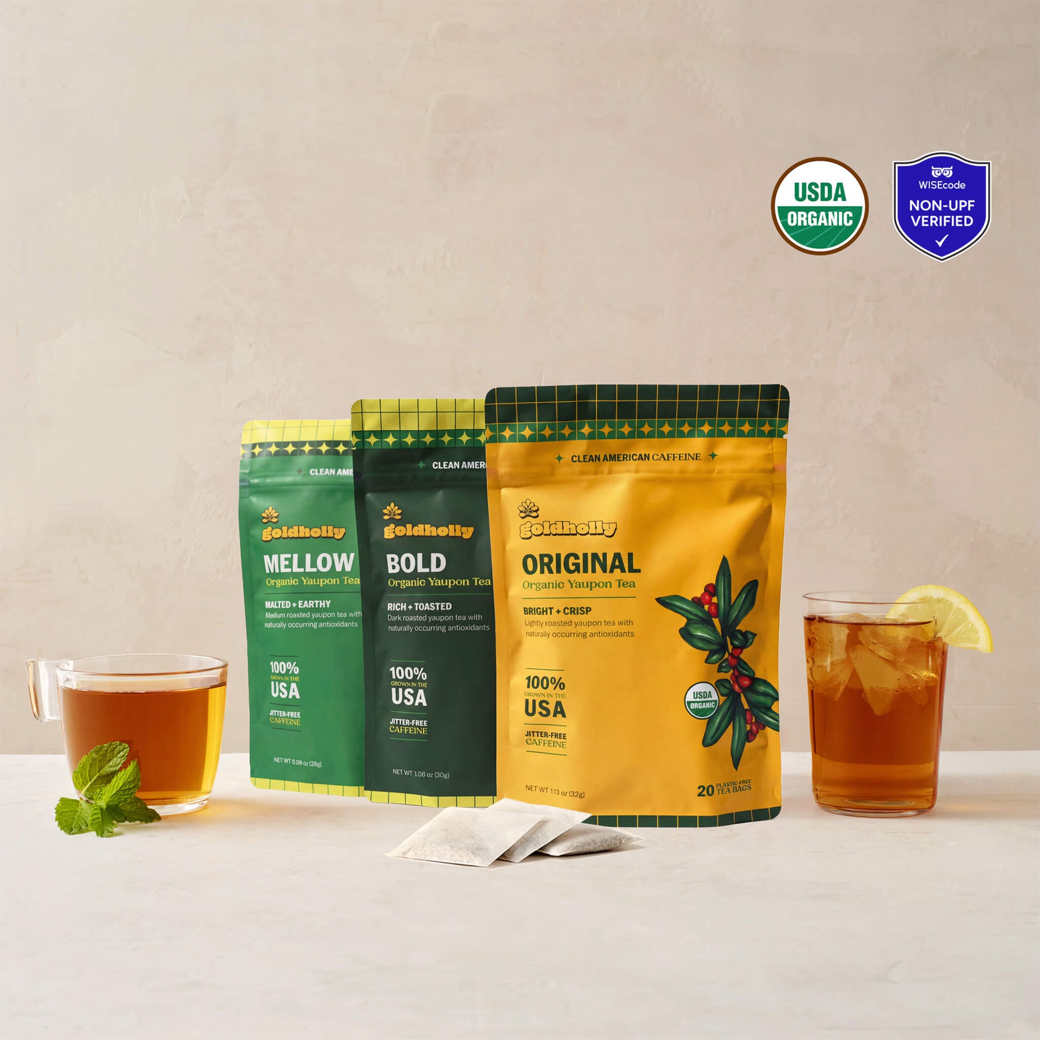 Goldholly variety bundle with Original, Bold, and Mellow organic yaupon tea pouches flanked by a warm cup of brewed tea and an iced glass with lemon, with three teabags. USDA Organic certified and WISEcode Non-UPF verified.--1