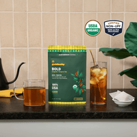 Goldholly Bold organic yaupon tea pouch on a kitchen counter with a mug of hot tea and a glass of iced tea; USDA Organic, Verified Non-UPF--1