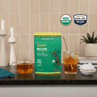 Goldholly Mellow organic yaupon tea pouch on a kitchen counter with a mug of hot tea and a glass of iced tea; USDA Organic, Verified Non-UPF--1