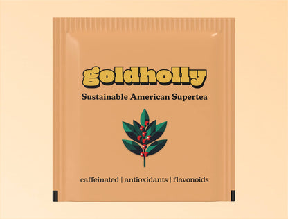 Individual tan-colored teabag packaging for Goldholly yaupon tea. The sachet features the yellow Goldholly logo at top, 'Sustainable American Supertea' tagline, and a geometric illustration of a yaupon holly branch with green leaves and red berries. At the bottom is the text 'caffeinated | antioxidants | flavonoids' describing the tea's properties.